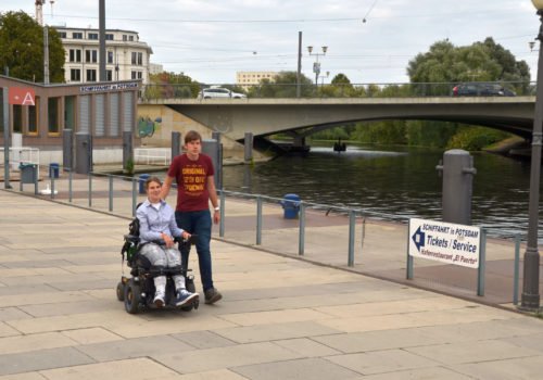 Lea Voitel und ihr Freund beim SPaziergang am Potsdamer Hafen. Sie sitzt im E-Rollstuhl, er leäuft rechts neben ihr.