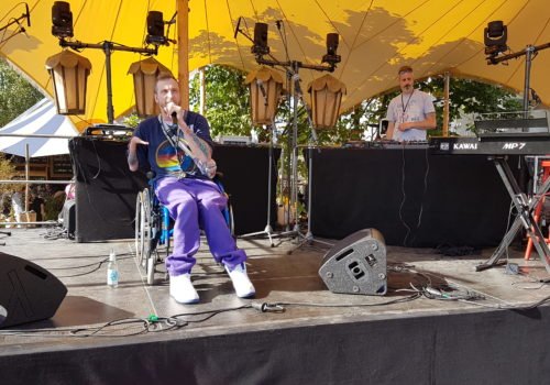 Mann im Rollstuhl singt mit Mikrofon in der Hand auf der Bühne