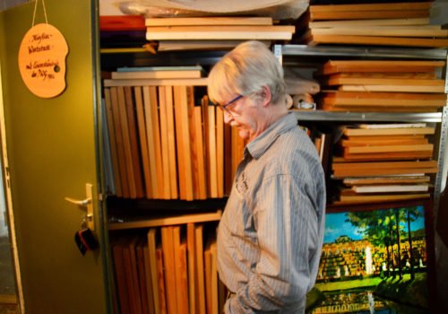 Foto: Maler Wieland Rödel im Profil im Keller vor einem Regal voller Ölgemälde