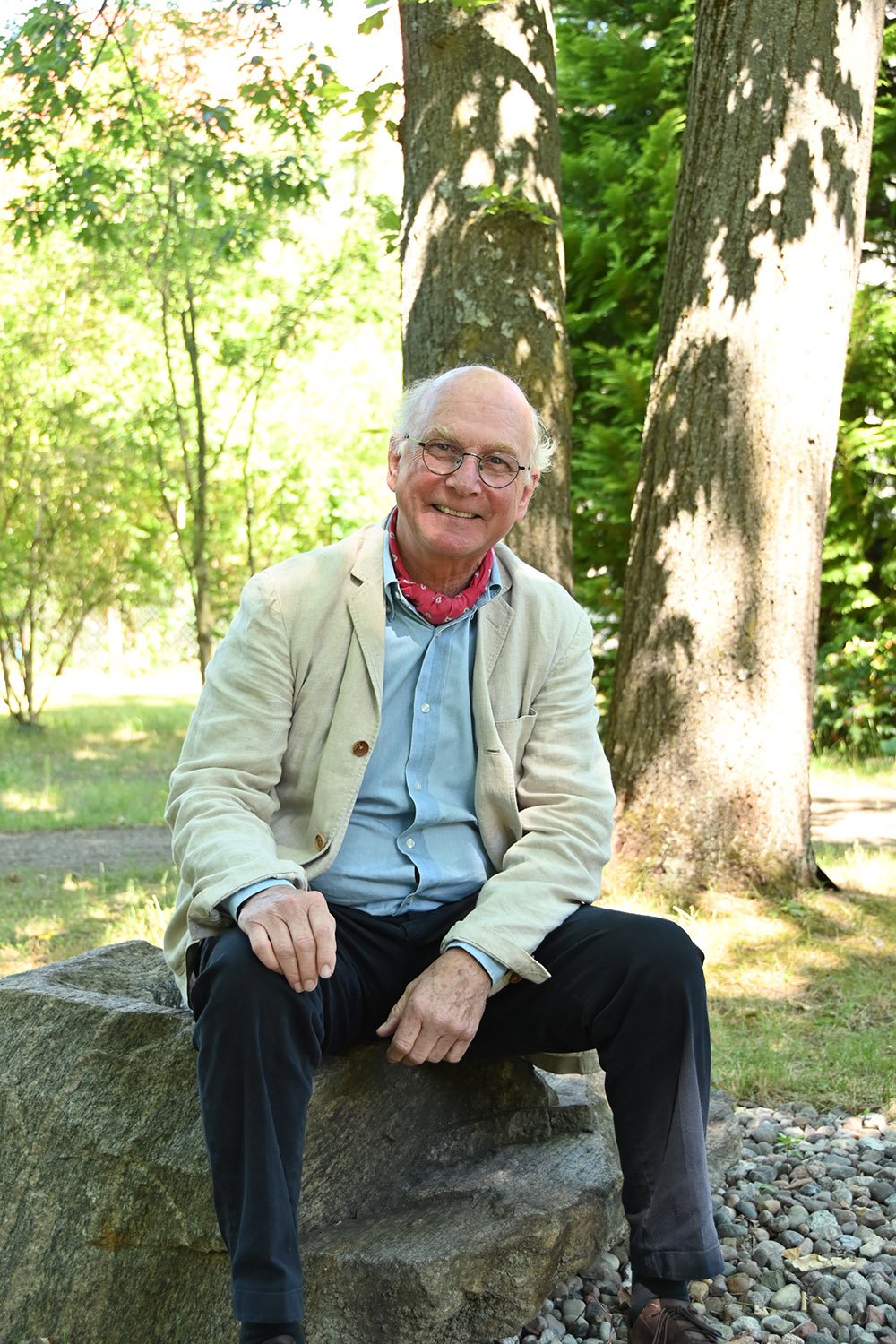 Guido Graf Henckel von Donnersmarck sitzt ganz leger auf einem großen Stein, dahinter Bäume und Sonnenschein.