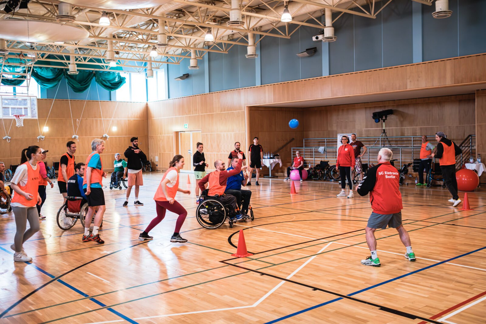 Menschen mit und ohne Behinderung, manche im Rollstuhl, spielen gemeinsam eine Ballsportart in einer Turnhalle.