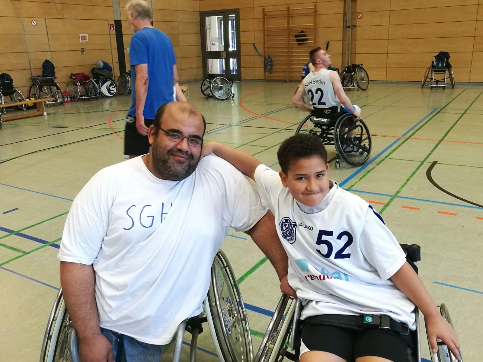 Ayman Mohsen posiert mit seinem Sohn in einer Sporthalle. Sein Sohn legt den Arm um seinen Vater - beide sitzen in einem Rollstuhl.