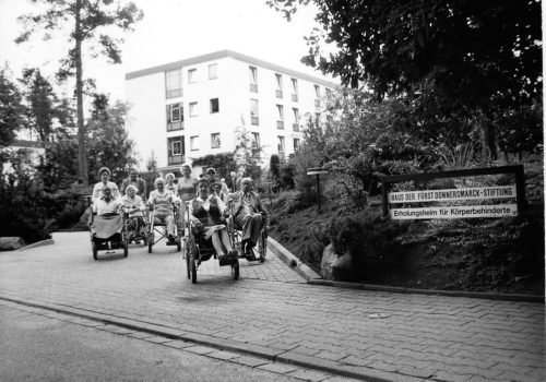 50 Jahre Heidehotel: Ein frühes Schwarz-Weiß-Foto vor dem Hotel in Bad Bevensen, davor eine Gruppe Rollstuhlfahrerinnen und fahrer.