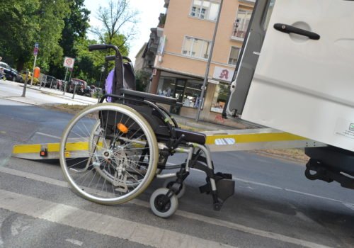 Ein leerer Rollstuhl steht vor einem Sprinter-Bus mit Rampe.