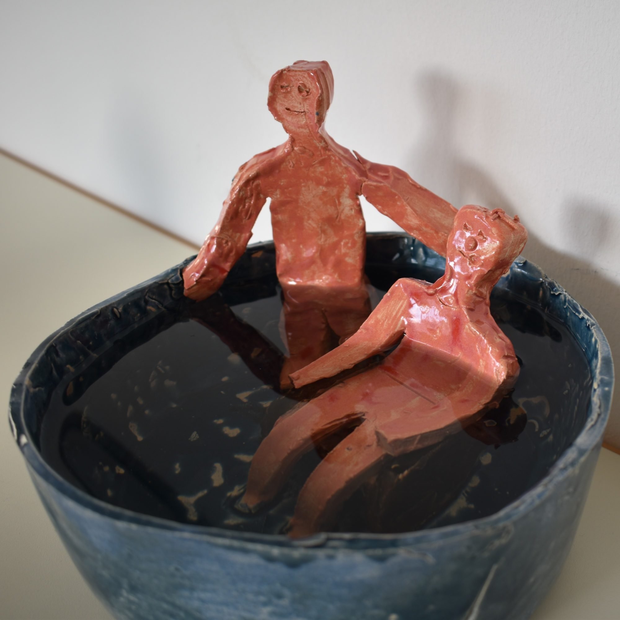 Zwei menschliche Gestalten aus Ton sitzen im Wasser in einer Schüssel aus Stein.