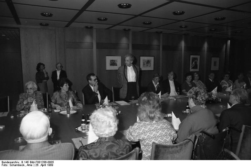 Ein historisches Schwarz-Weiß-Bild: Lieselotte Berger stehend an einem Tisch mit vielen anderen behinderten und nicht-behinderten Personen.