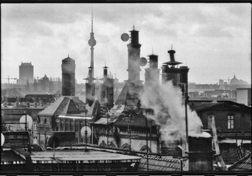 Schwarz-Weiß-Foto über den Dächern Berlins: Die Schornsteine der alten Mälzerei in Pankow sind zentral im Bild zu sehen, drumherum weitere Dächer und im Hintergrund der Fernsehturm