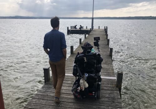 Marcel Renz fährt beim Camping im E-Rollstuhl über einen Steg am Starnberger See