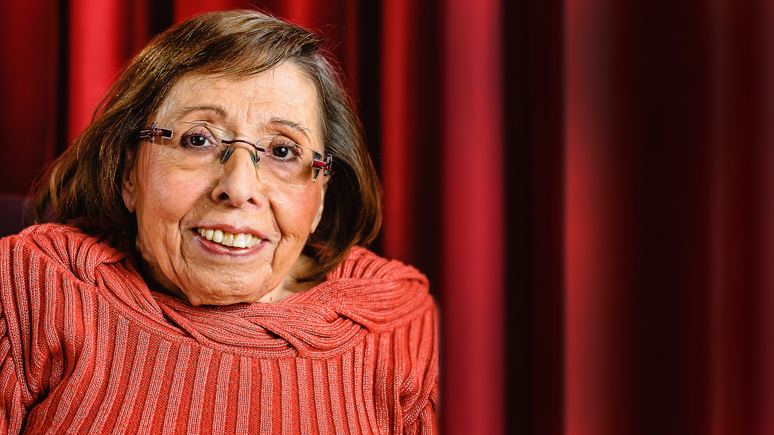 Foto: Portrait von Ingrid Koch, lachend vor einem roten Vorhang