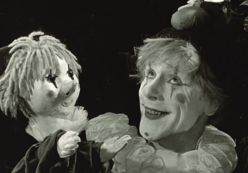Ein geschminkter Clown mit einer Clown-Handpuppe. Scan eines Schwarzweißfotos.