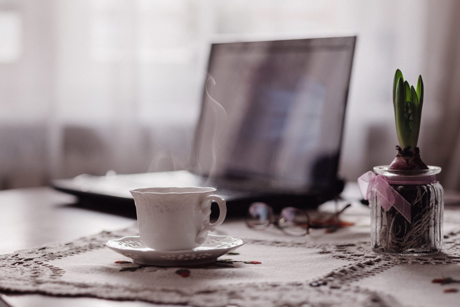 Ein Laptop und eine Tasse Kaffee auf einem Tisch mit Tischdecke.