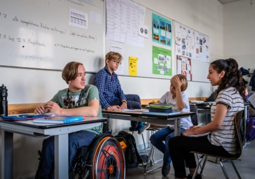 Inklusion an Schulen: Eine Schulklasse, vorne links am Tisch sitzt ein Junge im Rollstuhl.