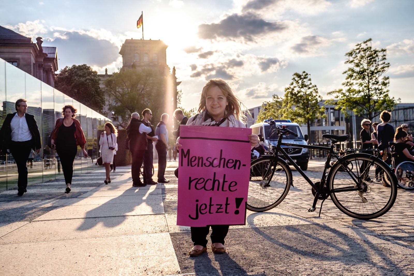 Eine Frau mit Kleinwuchs demonstriert in Berlin, vor dem Bundestag. Sie hält ein Plakat in den Händen auf dem steht: "Menschenrechte jetzt!".