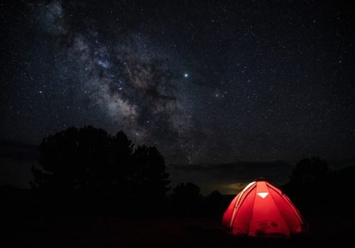 Traumvorstellung für Camping mit Rollstuhl: Ein rotes Zelt auf einer Waldlichtung und klarer Sternenhimmel.