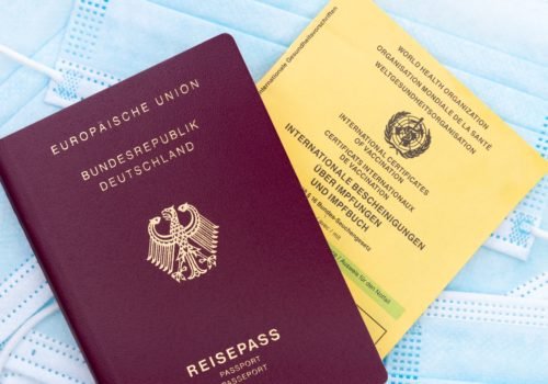 Ein deutscher Reisepass und ein Impfpass liegen auf einem Haufen OP-Masken.